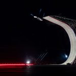 Tesla Roadster komt ondersteboven over de top van de gebogen schans, met witte stuwstralen uit de carrosserie, in het donker tijdens de presentatie.