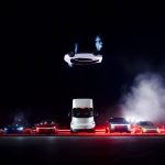Tesla Roadster zweeft ondersteboven op stuwstralen boven een rij Tesla's: een blauwe Model 3, een rode Model Y, de Tesla Semi, de Cybertruck en een goudkleurige Cybercab.