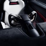 Stuur met koperkleurige schakelpeddels op een zwarte stuurkolom, voor een witte kuipstoel met rood verlicht Roadster-logo in de hoofdsteun.