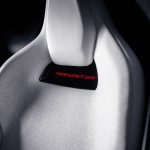Close-up van een witte kuipstoel met geperforeerd patroon en het rood oplichtende woord Roadster onder de hoofdsteun.