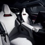 Interieur van de Tesla Roadster met twee witte geperforeerde kuipstoelen, zwarte veiligheidsgordels, een brede middenconsole en het middenscherm.