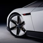 Voorwiel van de witte Tesla Roadster met stervormige velg, een Pirelli P Zero Trofeo RS-band en een carbon dorpel, in een donkere studio.