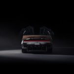 Achteraanzicht van de Tesla Roadster in een donkere studio, met beide deuren omhoog geopend, uitgeklapte spoiler en rode lichtbalk.