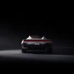 Achteraanzicht van de Tesla Roadster in een donkere studio, met ingeklapte spoiler, rode lichtbalk, kentekenplaat RDSTR en vier mondstukken.