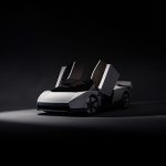 Witte Tesla Roadster schuin van voren in een donkere studio, met beide deuren omhoog geopend en de achterspoiler uitgeklapt.