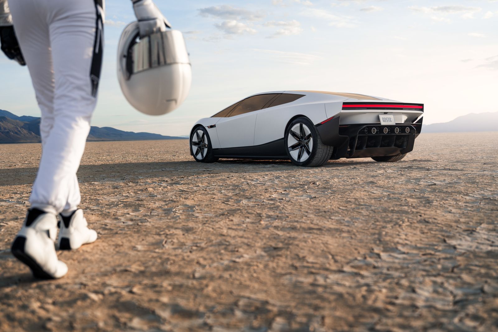 Coureur in wit racepak met helm in de hand loopt op een droge zoutvlakte naar de witte Tesla Roadster, met bergen aan de horizon.