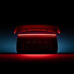 Silhouet van de achterkant van de Tesla Roadster met rood verlichte spoiler en lichtbalk, tegen een blauw verlichte achtergrond.