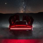 Tesla Roadster van achteren met beide deuren omhoog geopend en rode verlichting, op een woestijnvlakte onder een sterrenhemel met de Melkweg.